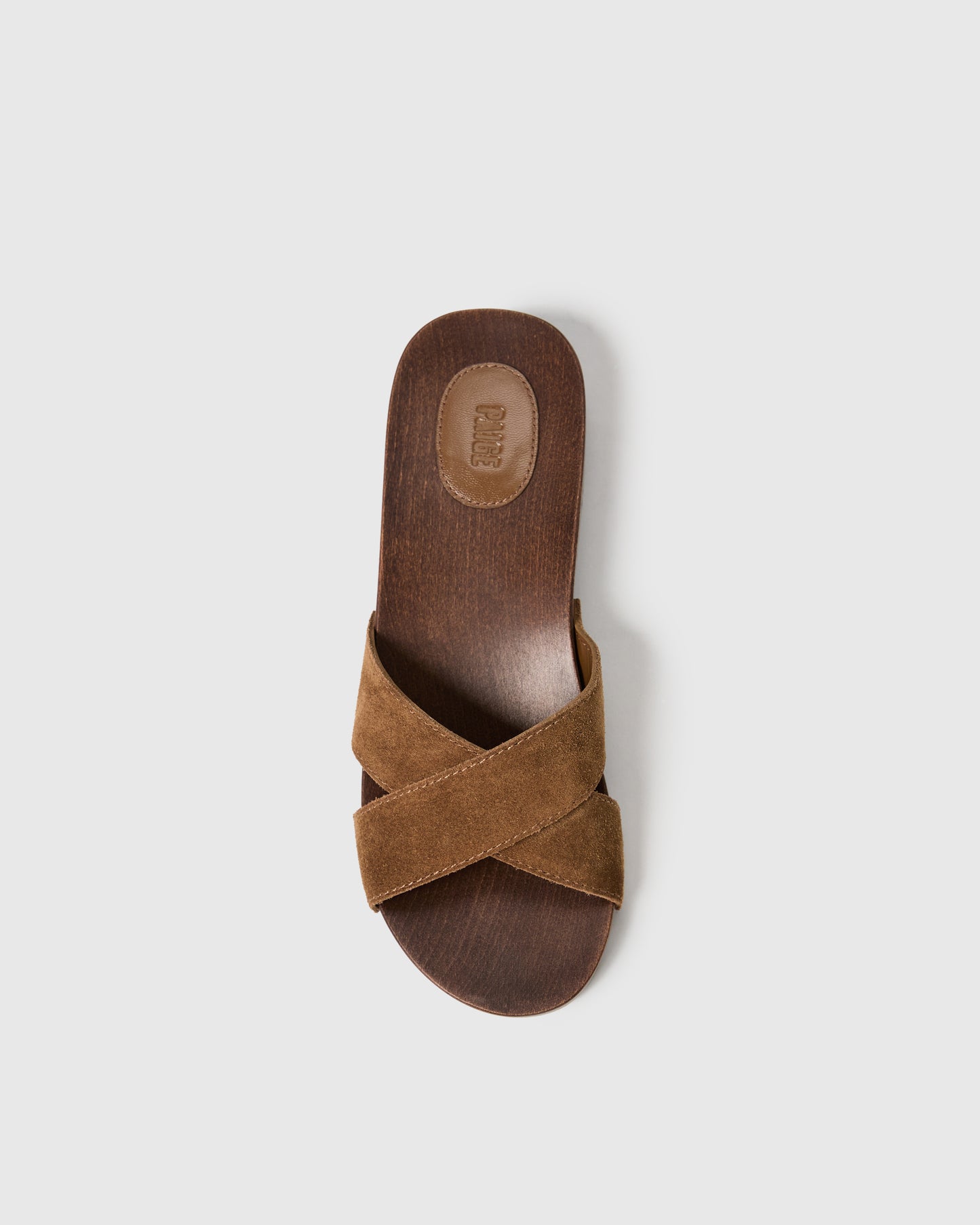 Brown sandal with criss-cross strap design on a light gray background