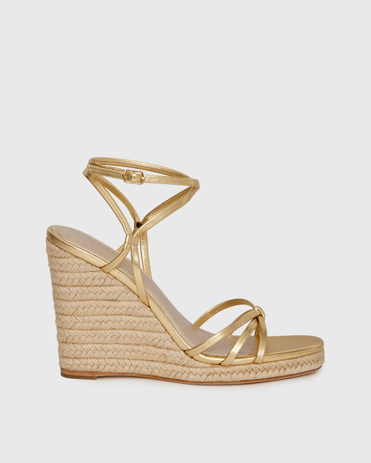 Gold wedge sandal with espadrille sole on a light gray background