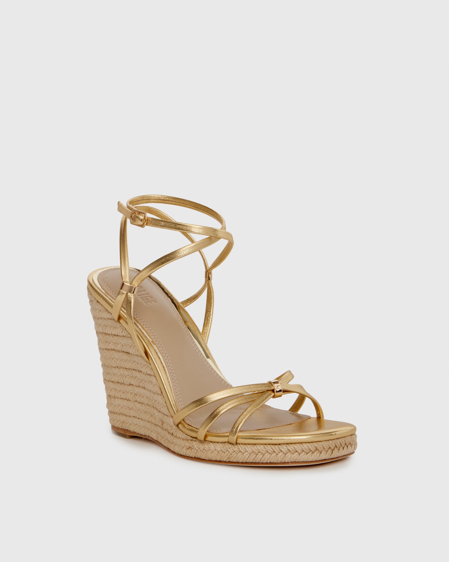 Gold wedge sandal with espadrille sole on a light gray background