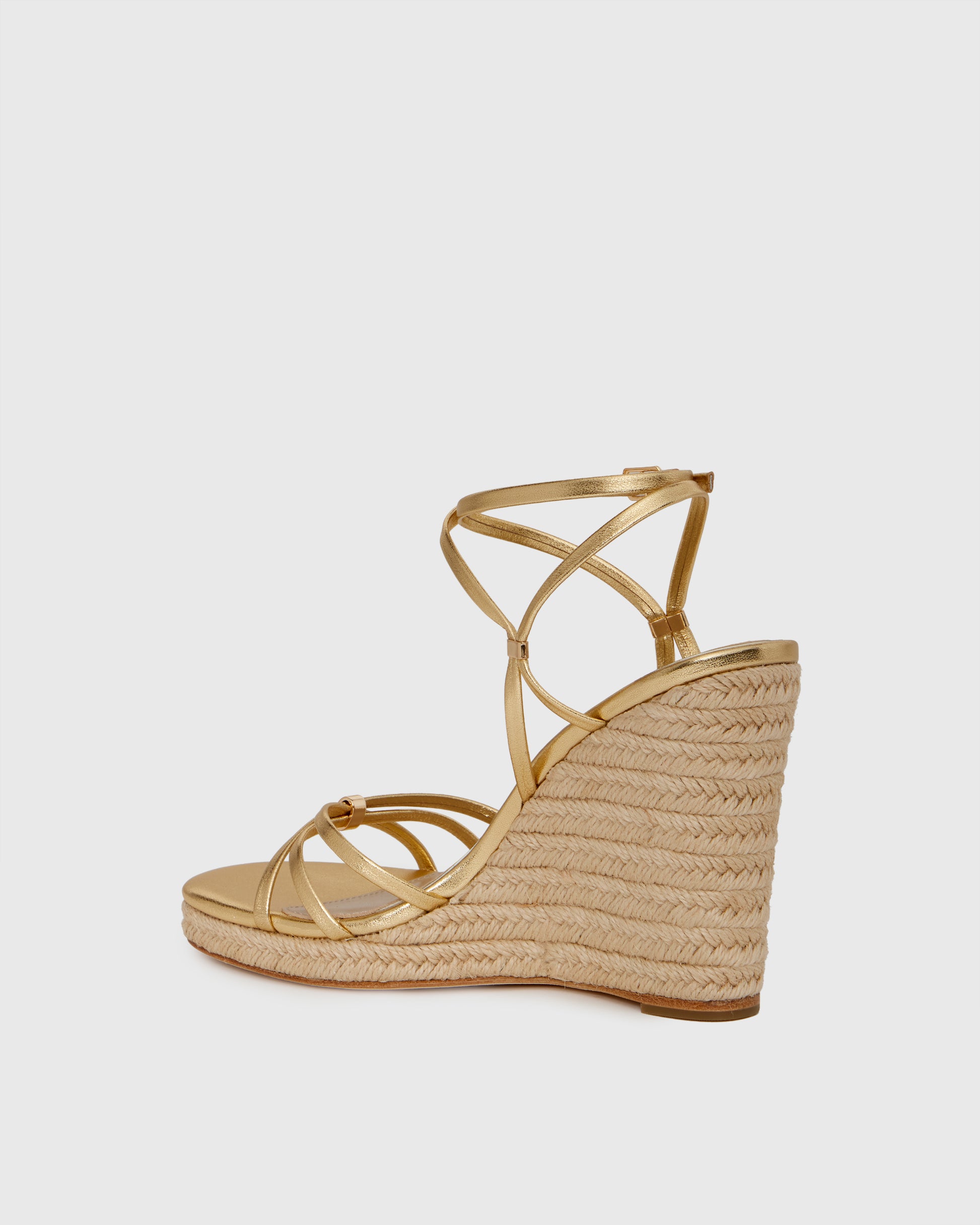 Gold wedge sandal with espadrille sole on a light gray background