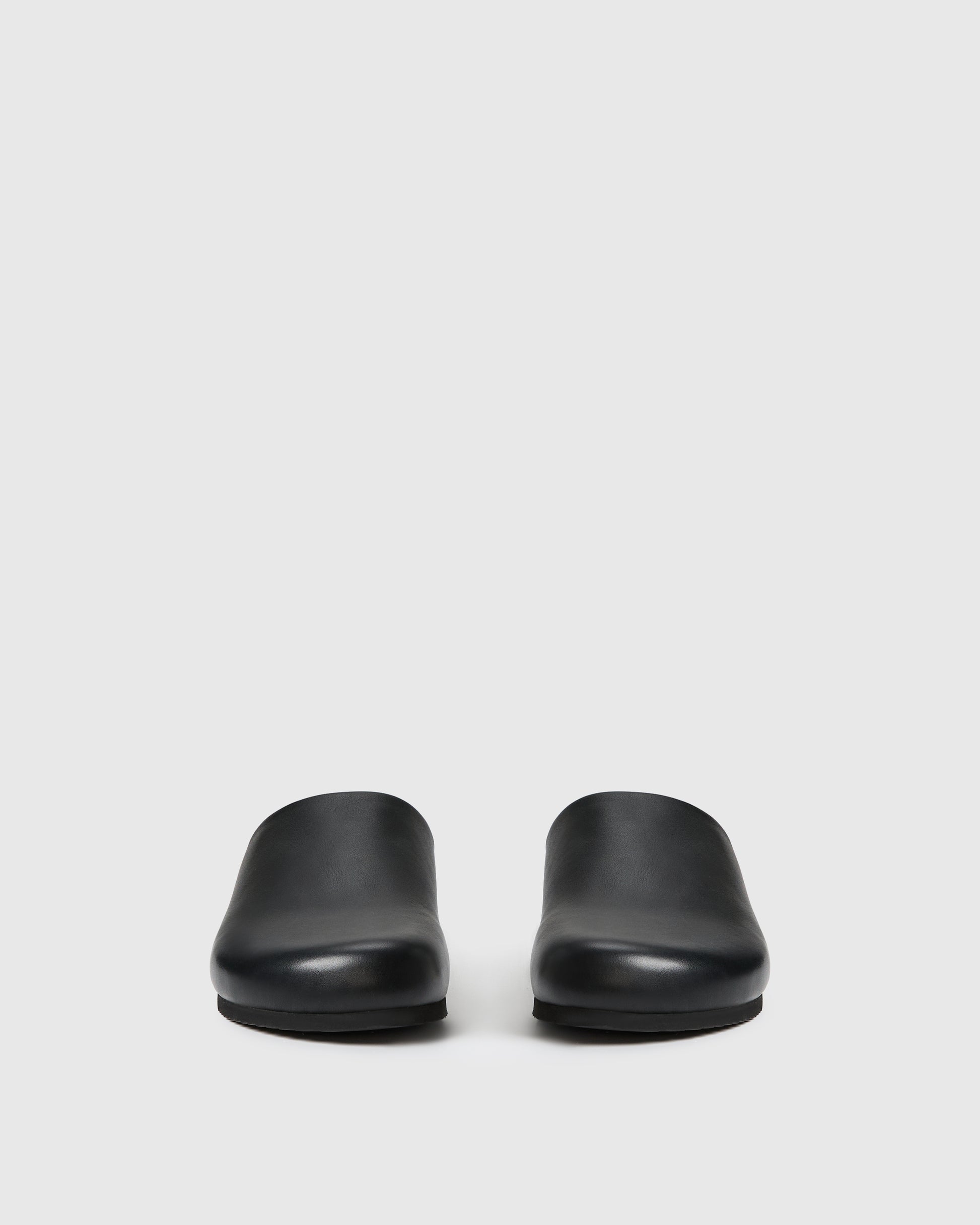 Black slip-on clog-style shoe with a smooth upper set against a white background.
