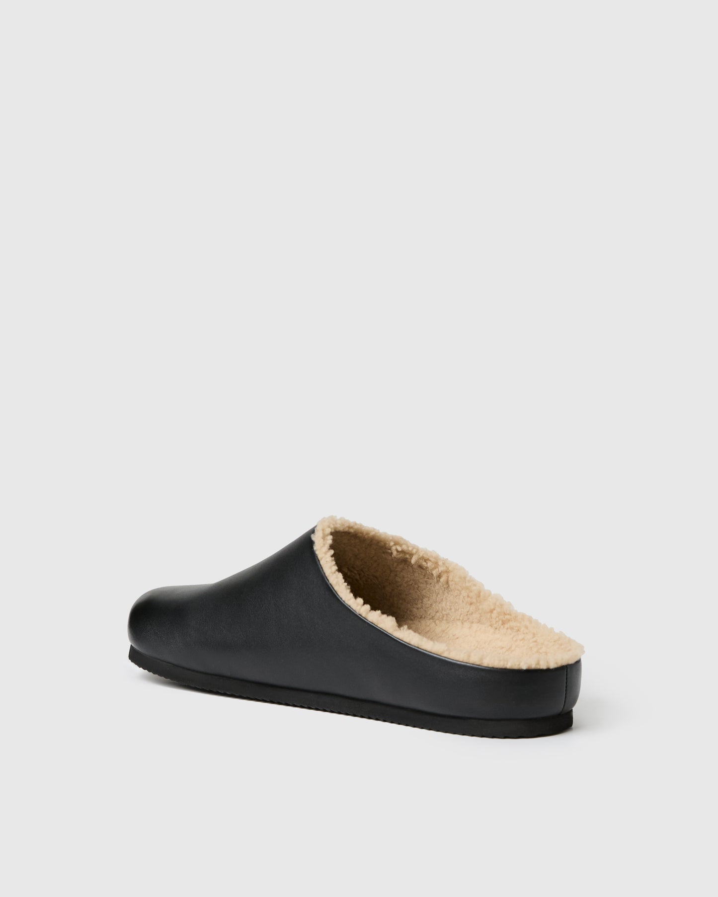 Black slip-on clog-style shoe with a smooth upper and plush shearling lining, set against a white background.