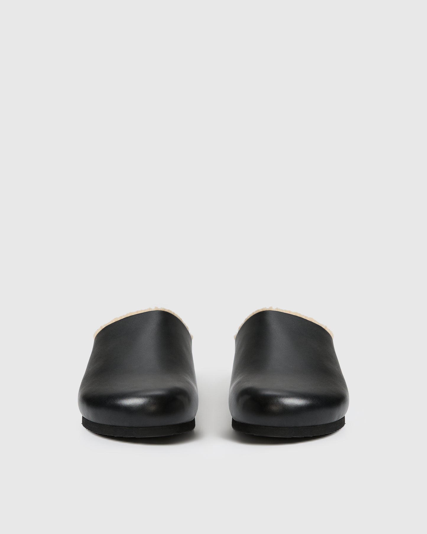 Black slip-on clog-style shoe with a smooth upper and plush shearling lining, set against a white background.