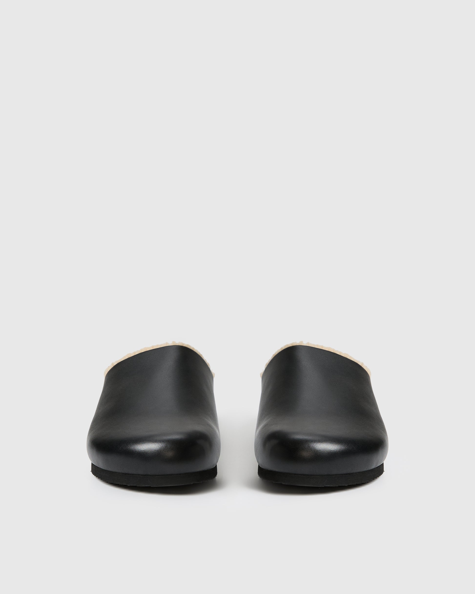Black slip-on clog-style shoe with a smooth upper and plush shearling lining, set against a white background.