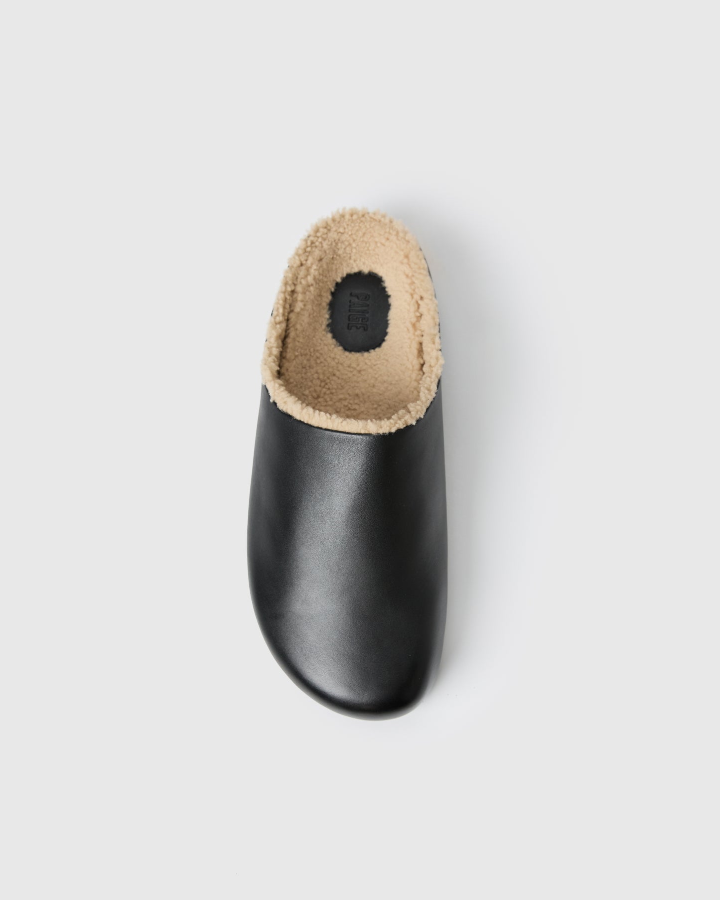 Black slip-on clog-style shoe with a smooth upper and plush shearling lining, set against a white background.